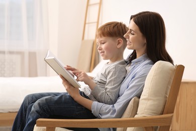 Photo of Mother reading book with her child on armchair at home