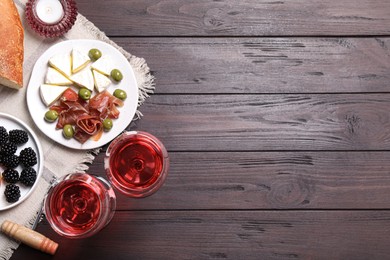 Glasses of delicious rose wine and snacks on wooden table, flat lay