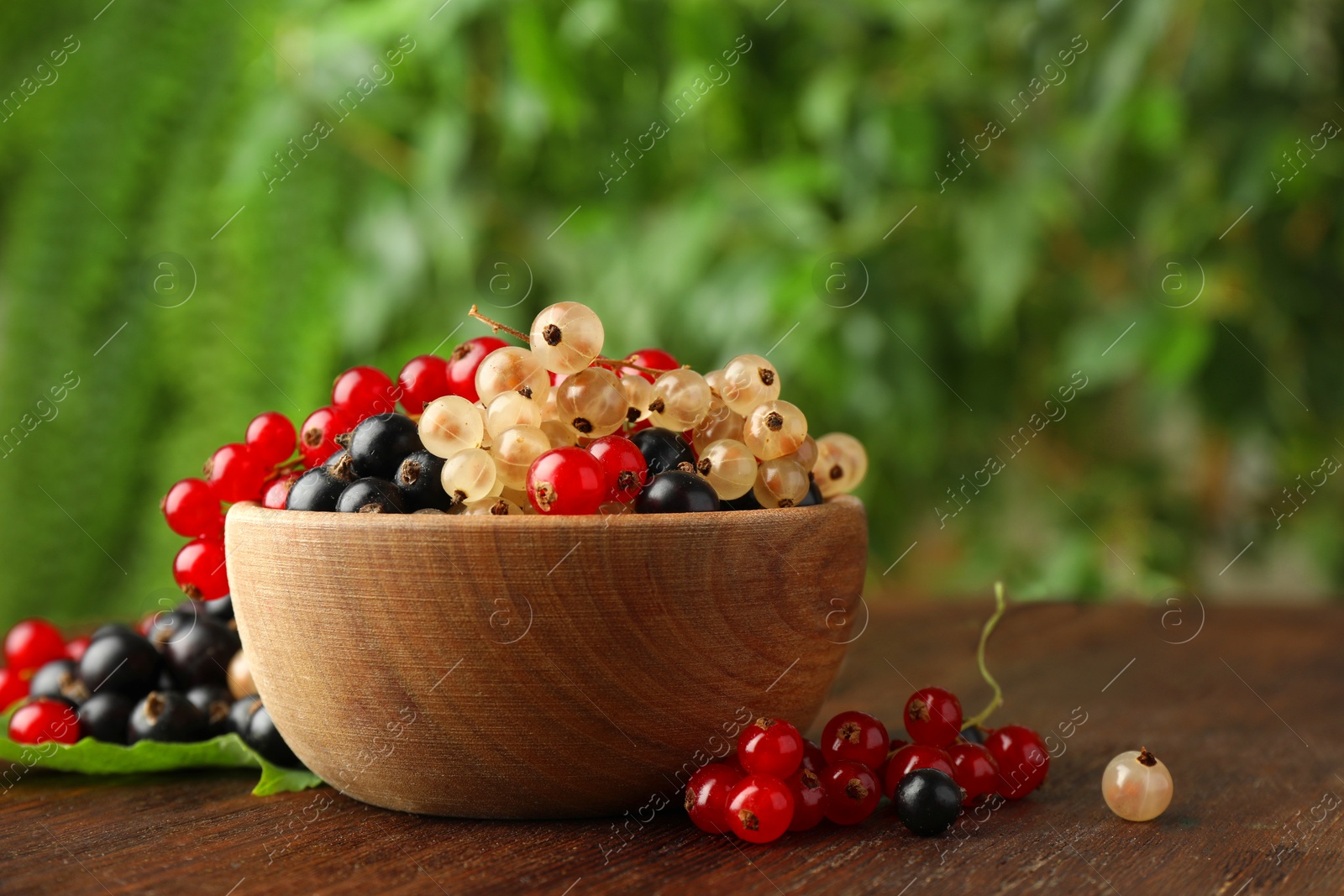 Photo of Different fresh ripe currants and green leaf on wooden table outdoors, space for text