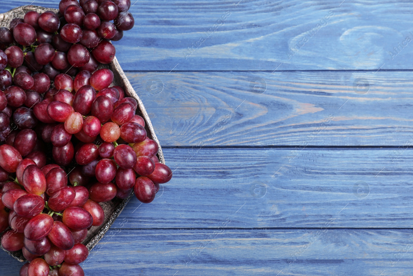 Photo of Fresh ripe juicy grapes on blue wooden table, top view. Space for text