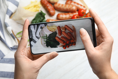 Photo of Blogger taking photo of grilled sausages with garnish at white table, closeup