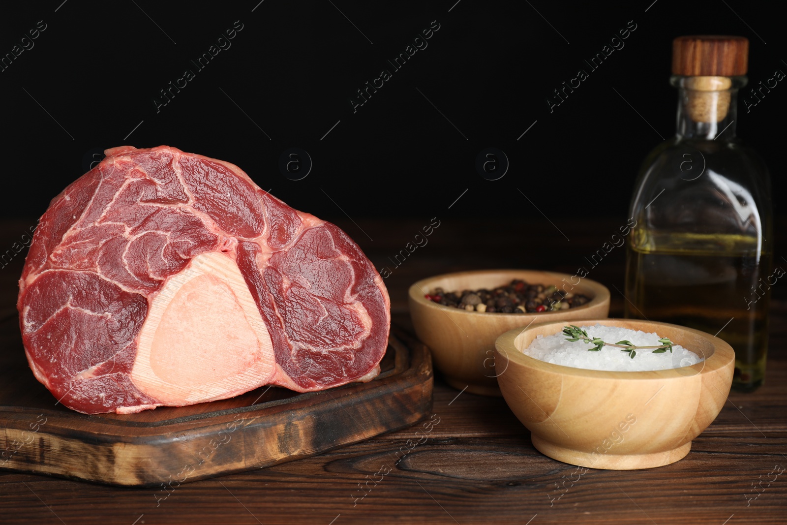 Photo of Piece of raw beef meat and spices on wooden table against black background, closeup