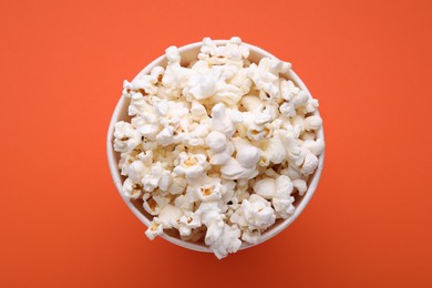 Bucket of tasty popcorn on orange background, top view