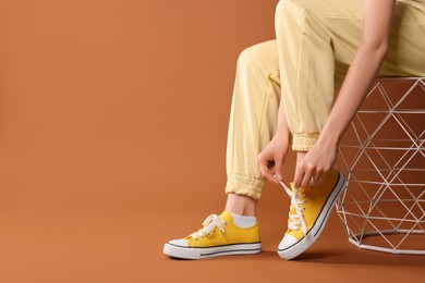 Photo of Woman tying shoelace of classic old school sneaker on brown background, closeup. Space for text