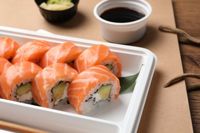 Food delivery. Delicious sushi rolls in plastic container on wooden table, closeup