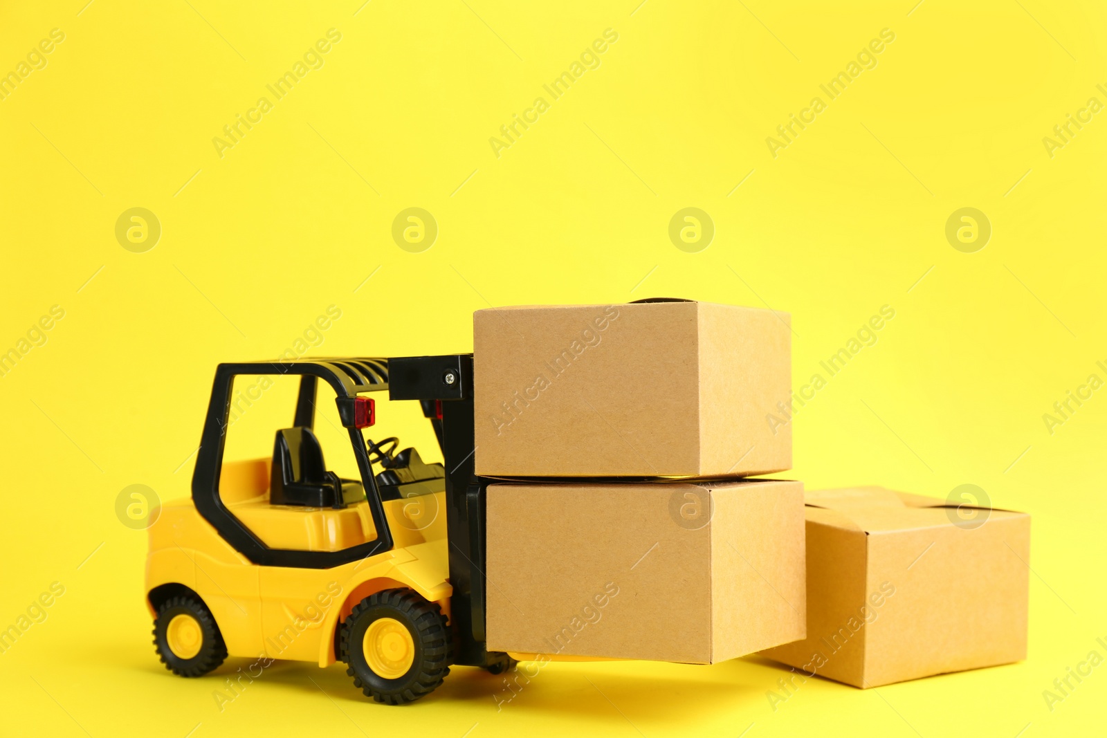 Photo of Forklift model and carton boxes on yellow background. Courier service