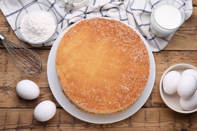 Plate with delicious sponge cake and ingredients on wooden table, flat lay