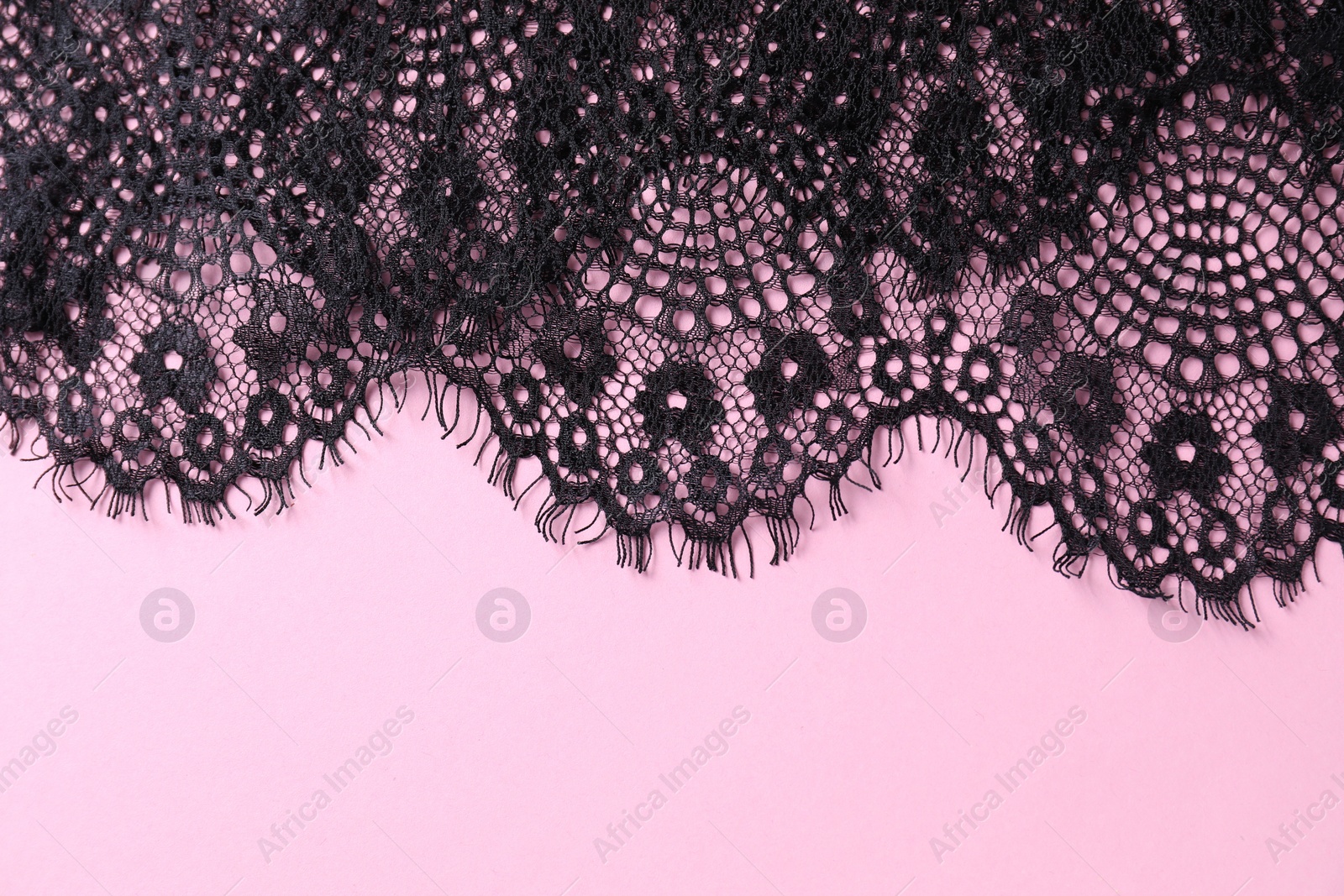 Photo of Black lace on pink background, top view. Space for text