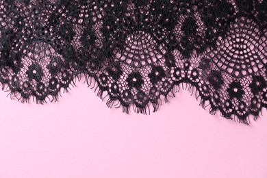 Black lace on pink background, top view. Space for text