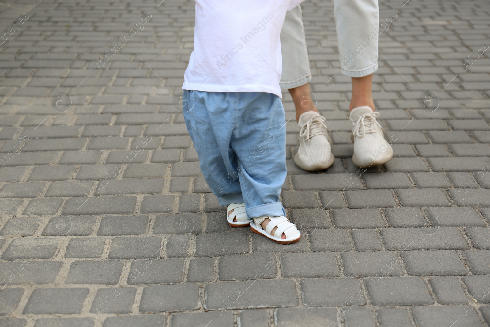 Photo of Mother supporting daughter while she learning to walk outdoors, closeup