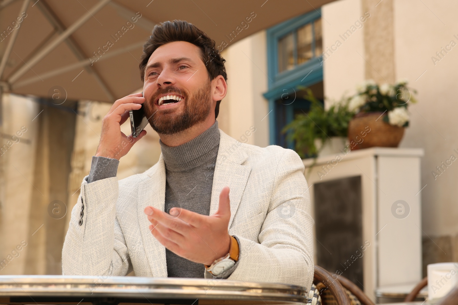 Photo of Handsome man talking on phone at table in outdoor cafe