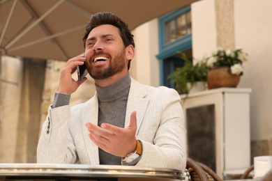 Handsome man talking on phone at table in outdoor cafe