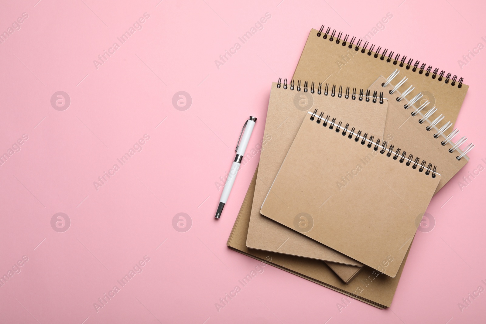 Photo of Stylish kraft notebooks and pen on pink background, flat lay. Space for text