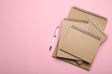 Stylish kraft notebooks and pen on pink background, flat lay. Space for text