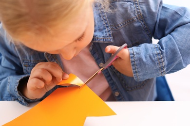 Photo of Little girl left-handed cutting construction paper at table, closeup
