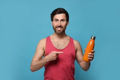 Photo of Man pointing at orange thermo bottle on light blue background