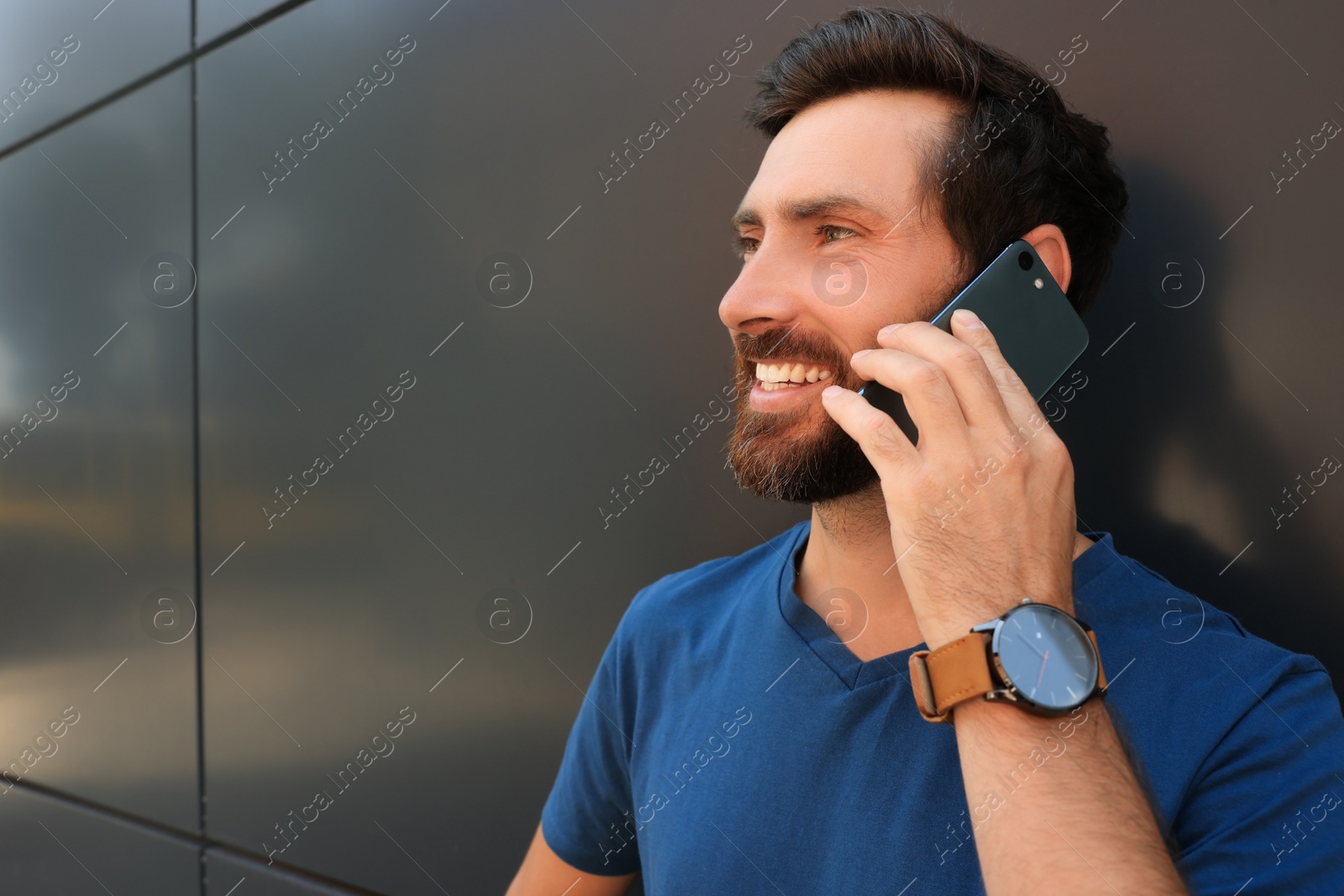 Photo of Happy man talking on phone near grey wall. Space for text