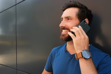 Photo of Happy man talking on phone near grey wall. Space for text