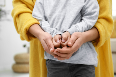 Photo of Mother holding hands with her child indoors, closeup. Happy family