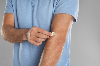 Photo of Man putting sticking plaster onto arm against light grey background, closeup