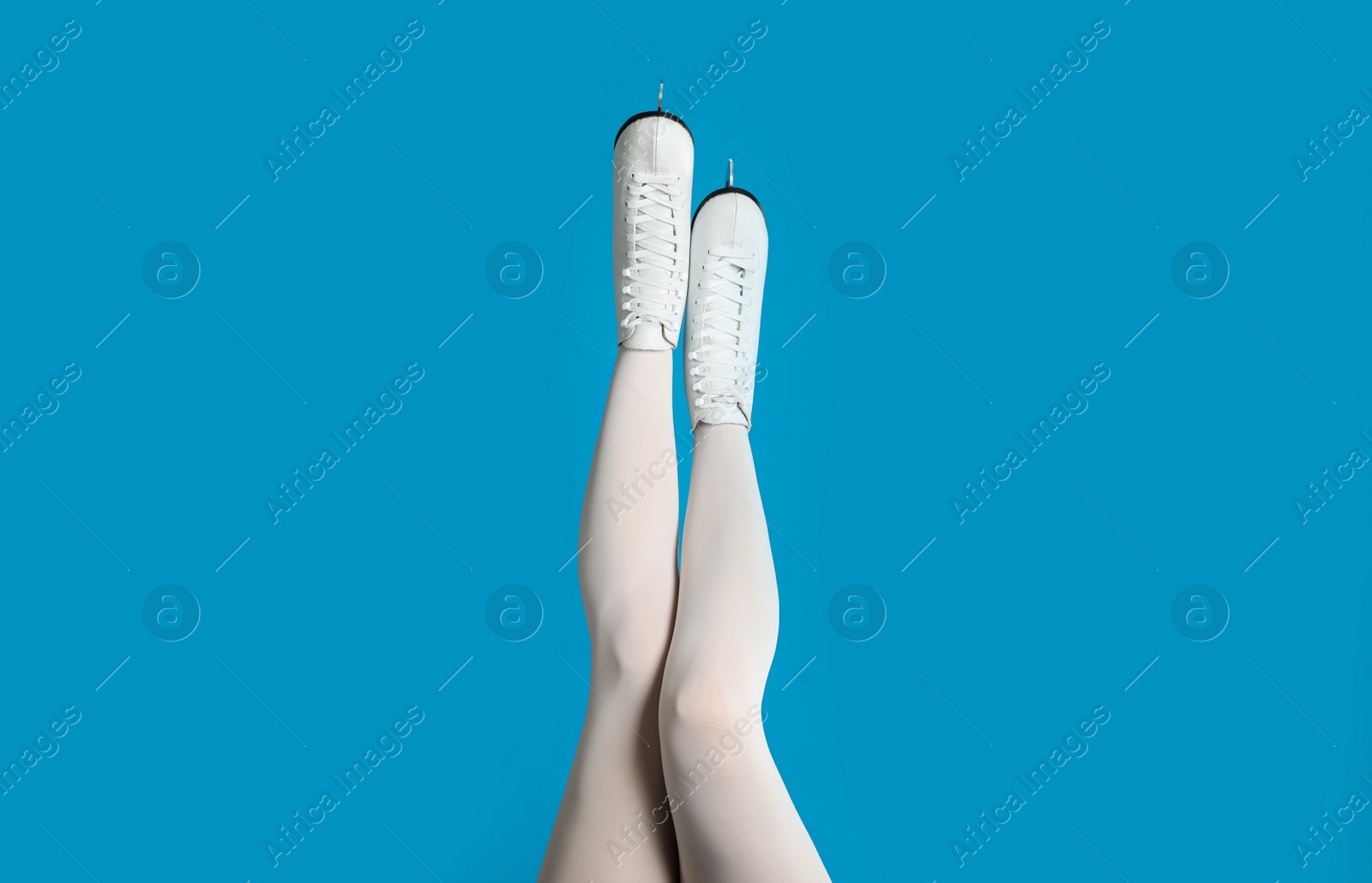 Photo of Woman in elegant white ice skates on light blue background, closeup of legs