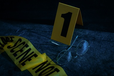 Photo of Glasses with tape and crime scene marker on stone table at night