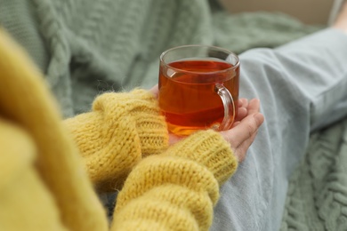 Woman with cup of tea sitting on plaid, closeup