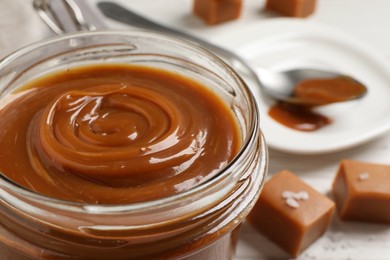 Photo of Yummy salted caramel in glass jar on table, closeup