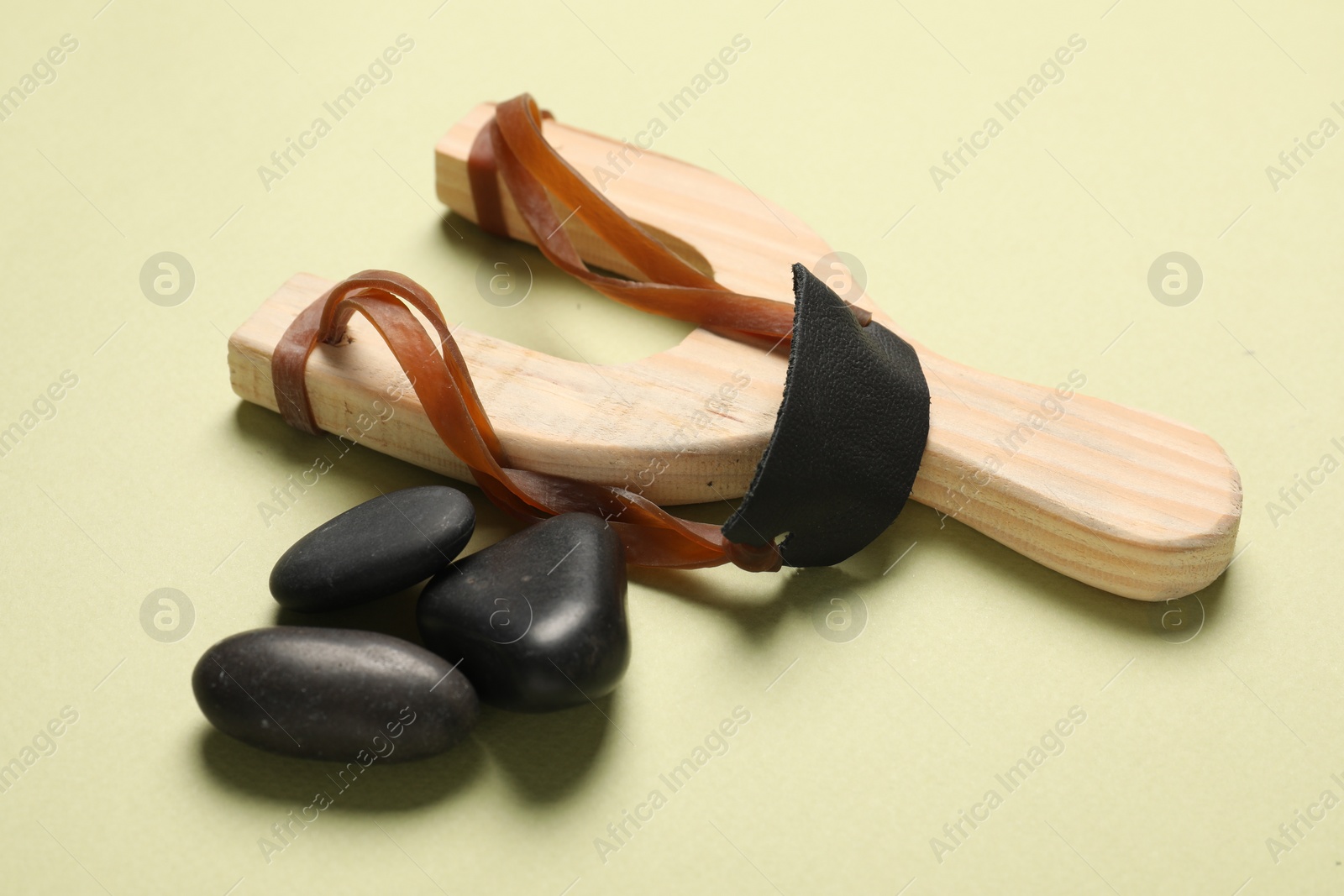 Photo of Wooden slingshot with pebble on light yellow background, closeup