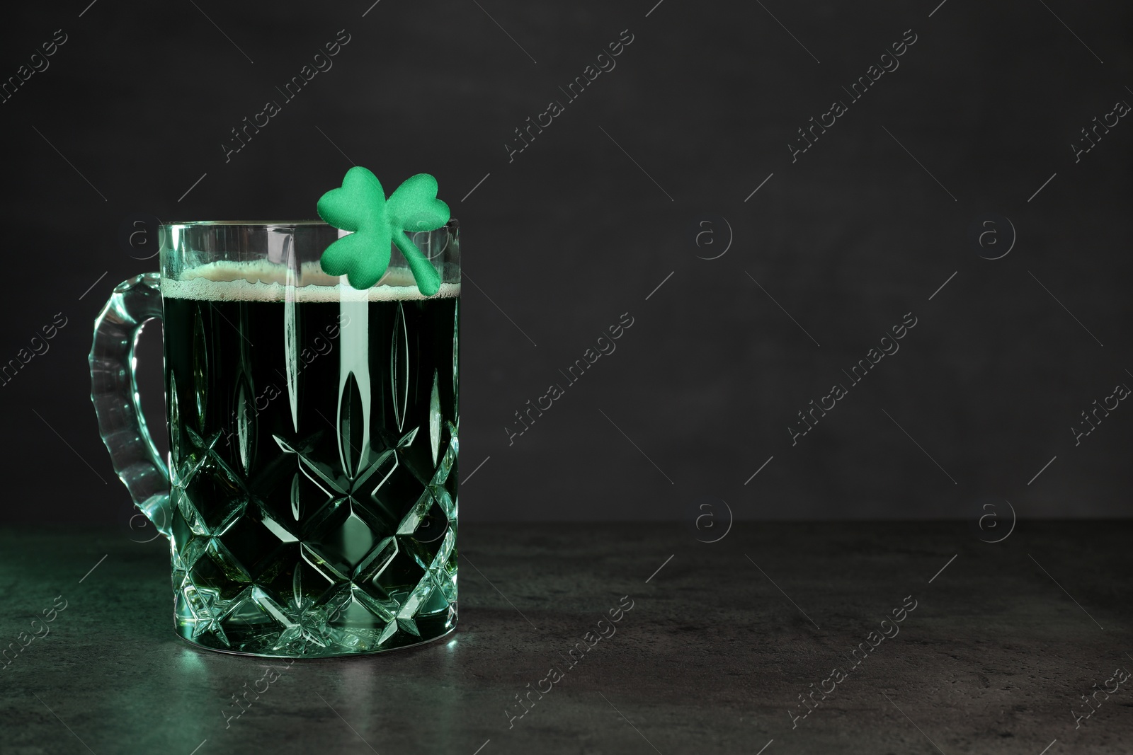 Photo of St. Patrick's day celebration. Green beer with decorative clover leaf on grey table. Space for text
