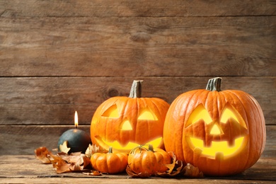 Photo of Scary jack o'lantern pumpkins, burning candle and fallen leaves on wooden background. Halloween decor
