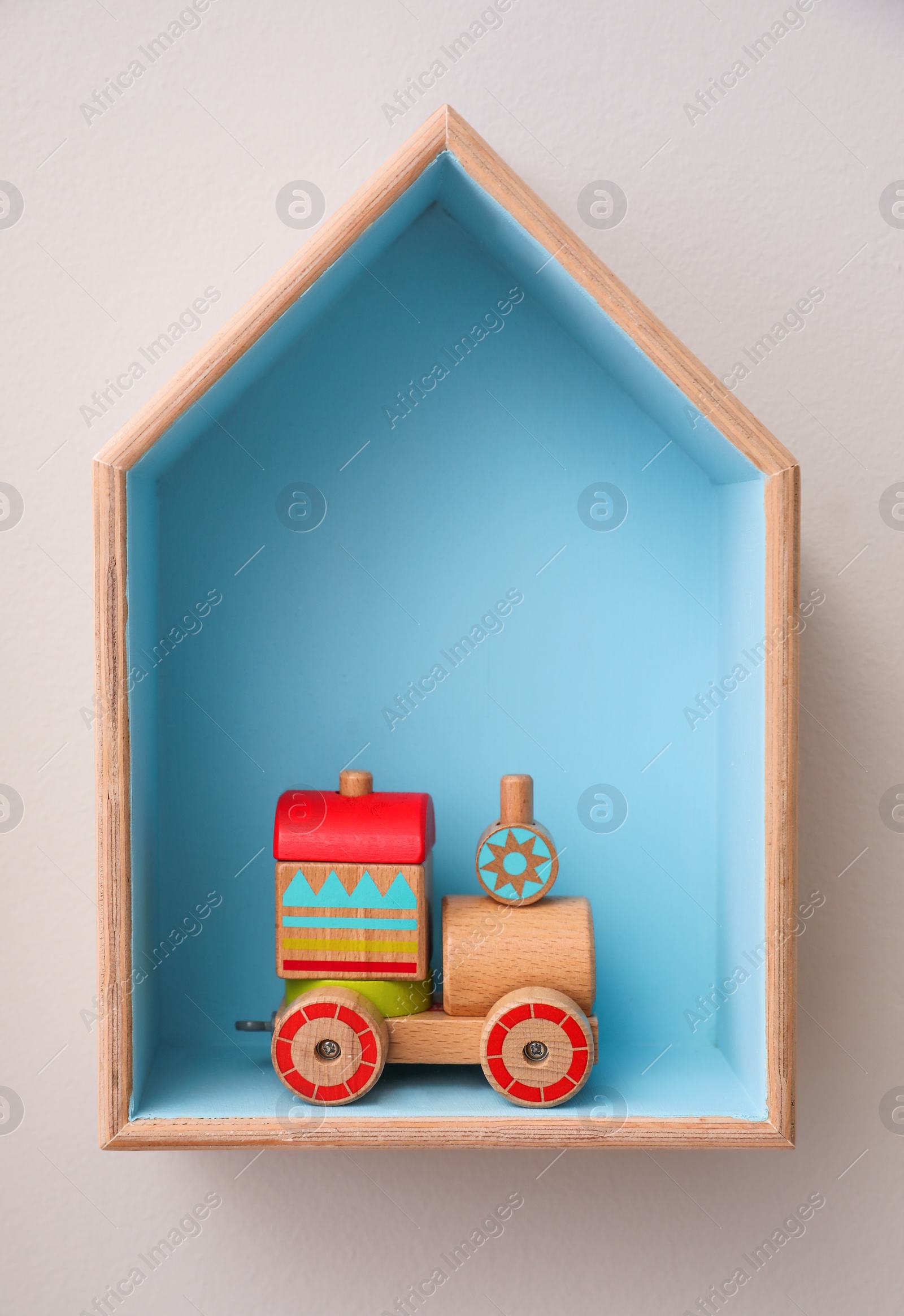 Photo of Stylish house shaped shelf with toy on white wall. Baby room interior design