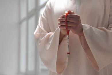 Photo of Muslim man with misbaha praying indoors, closeup. Space for text