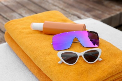 Photo of Beach towels, sunglasses and sunscreen on sunbed near outdoor swimming pool, closeup. Luxury resort