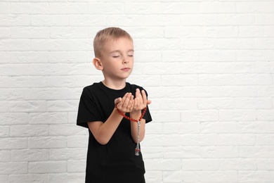 Little Muslim boy praying near brick wall