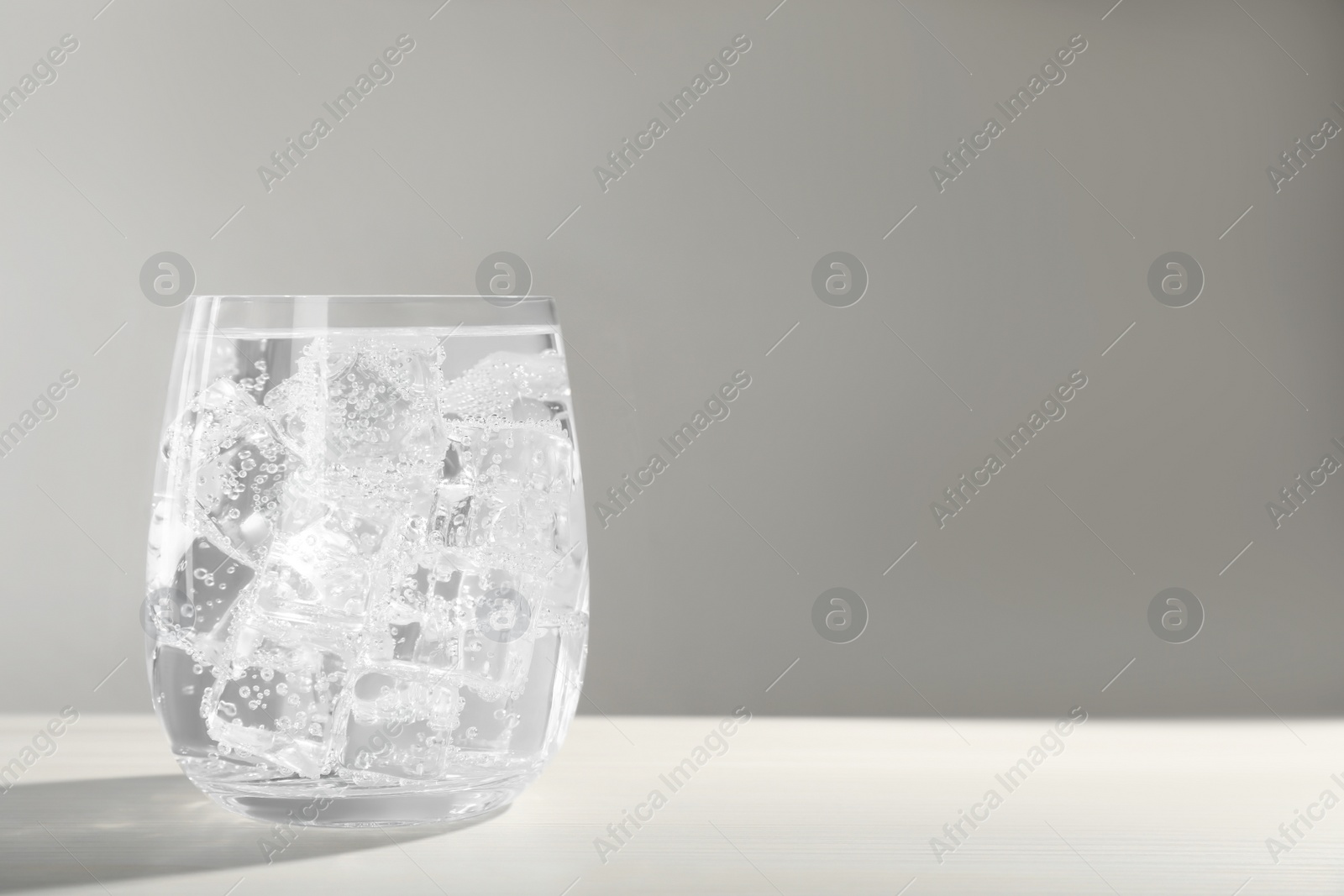 Photo of Glass of soda water with ice on white wooden table. Space for text