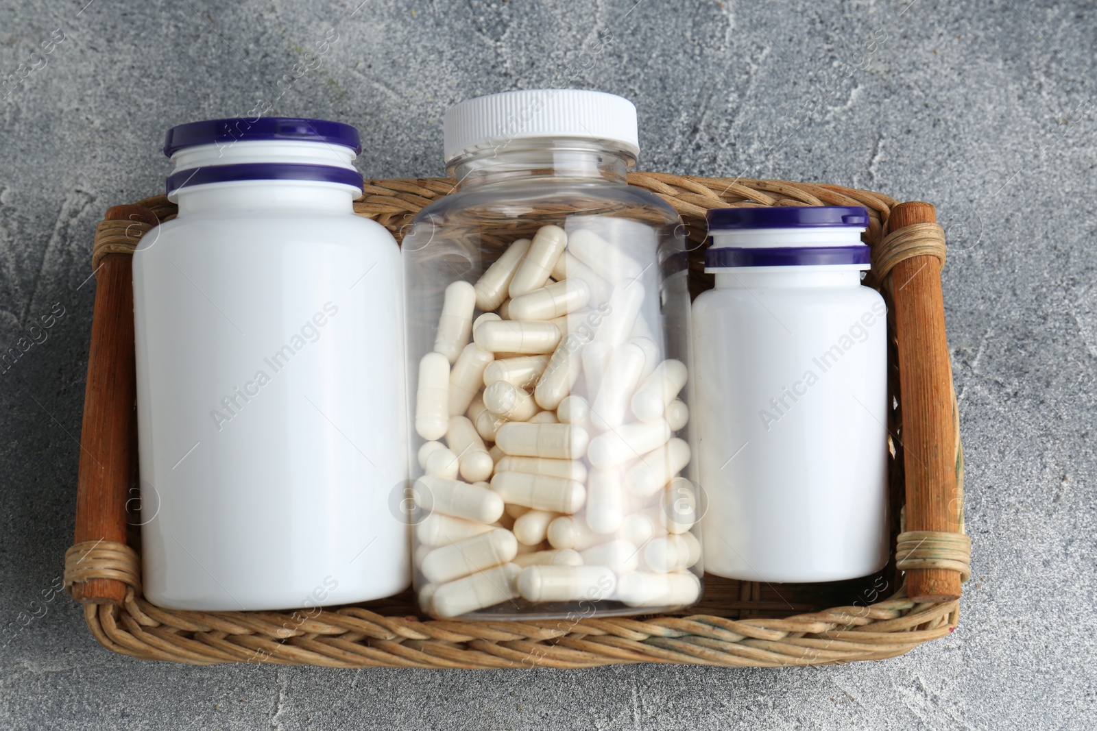 Photo of Medical bottles with pills in wicker tray on light gray textured table, top view