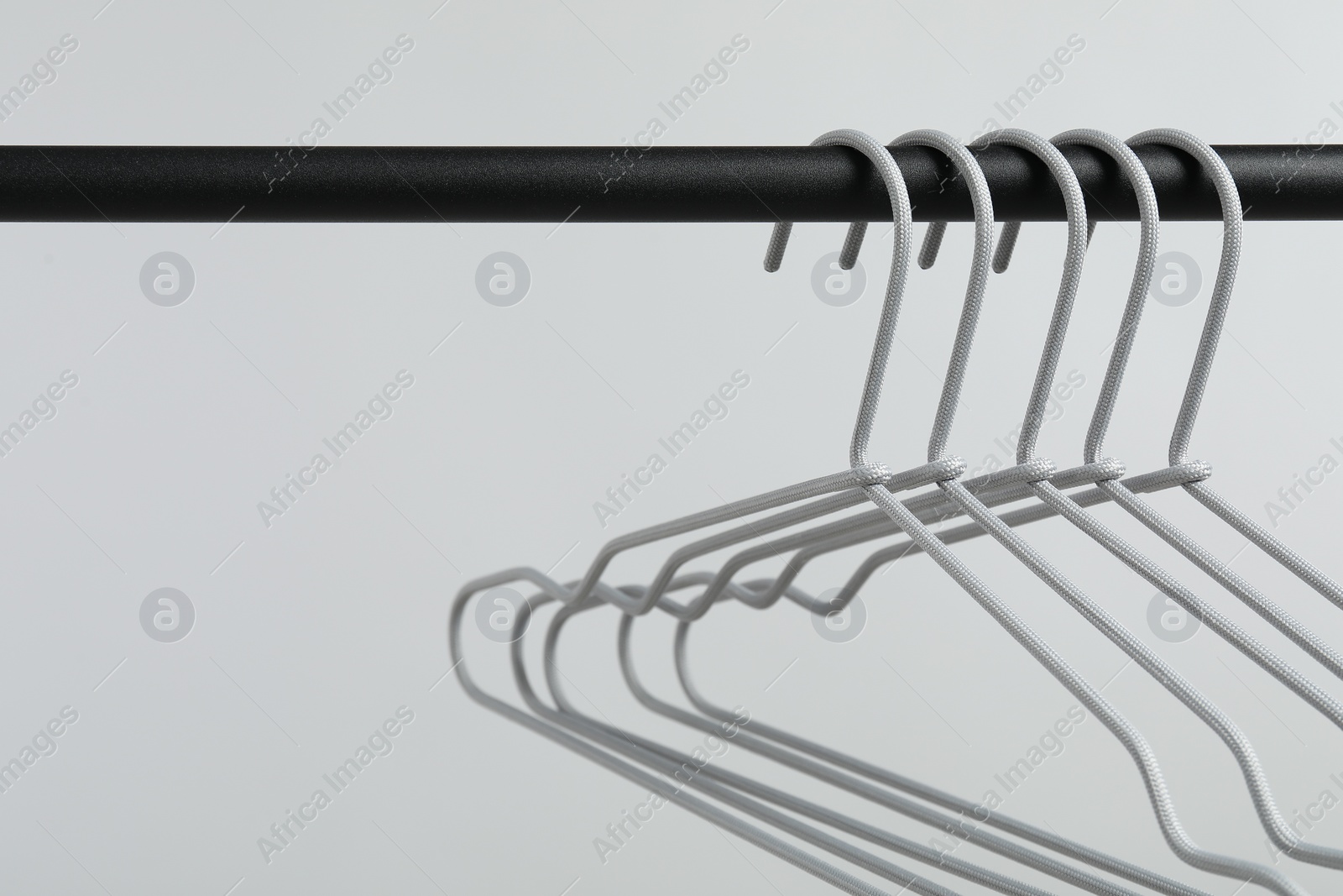 Photo of Empty clothes hangers on black rack against light grey background, closeup. Space for text