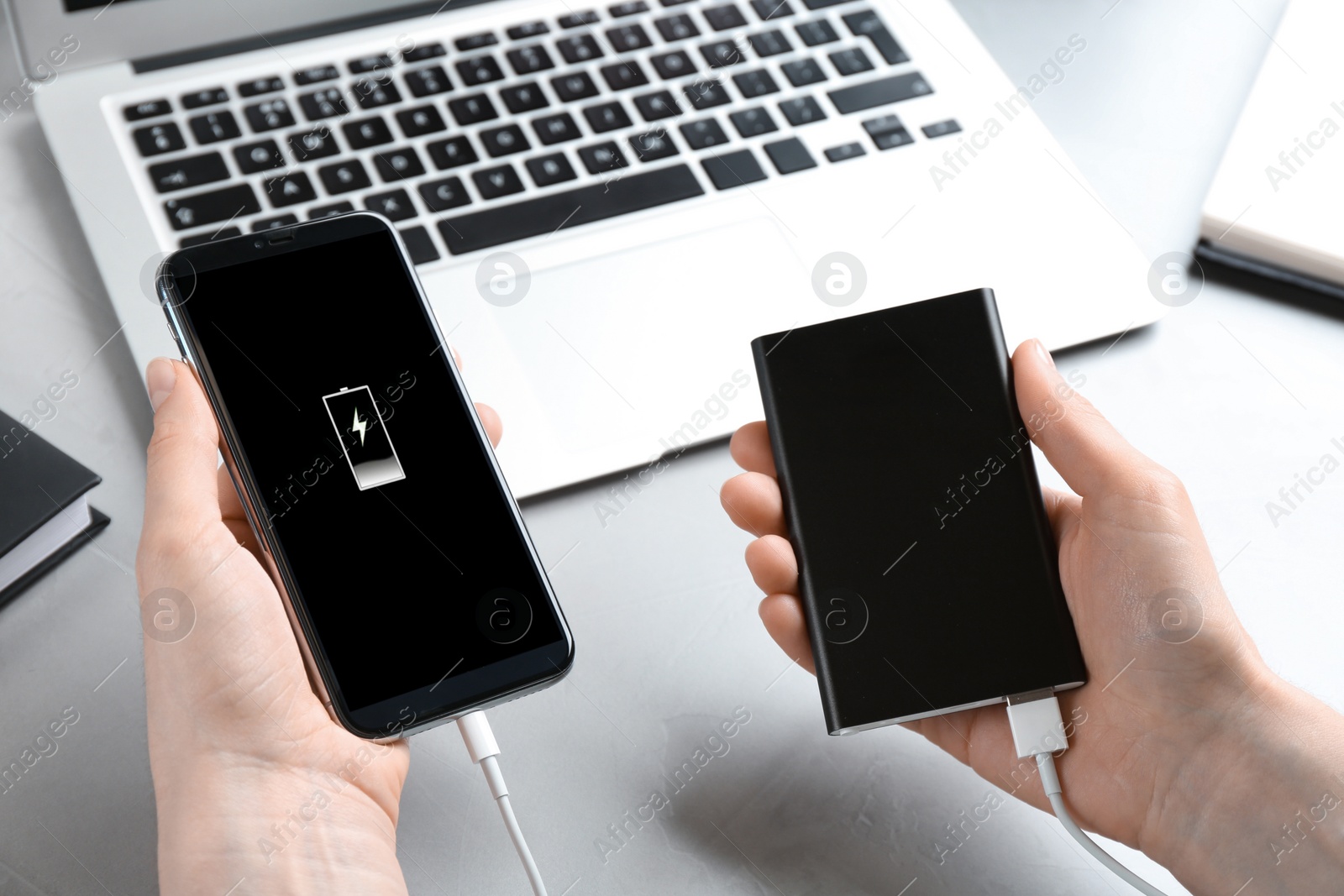 Photo of Woman charging mobile phone with power bank at light grey stone table, closeup