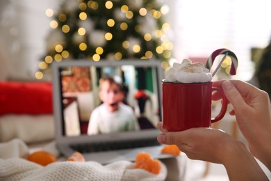 Photo of MYKOLAIV, UKRAINE - DECEMBER 25, 2020: Woman with sweet drink watching Home Alone movie on laptop indoors, closeup. Cozy winter holidays atmosphere