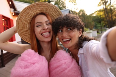 Photo of Happy friends with cotton candies taking selfie outdoors
