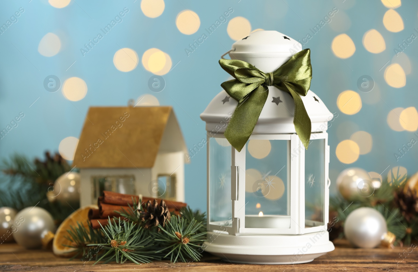 Photo of Christmas lantern with burning candle and festive decor on wooden table against blurred lights