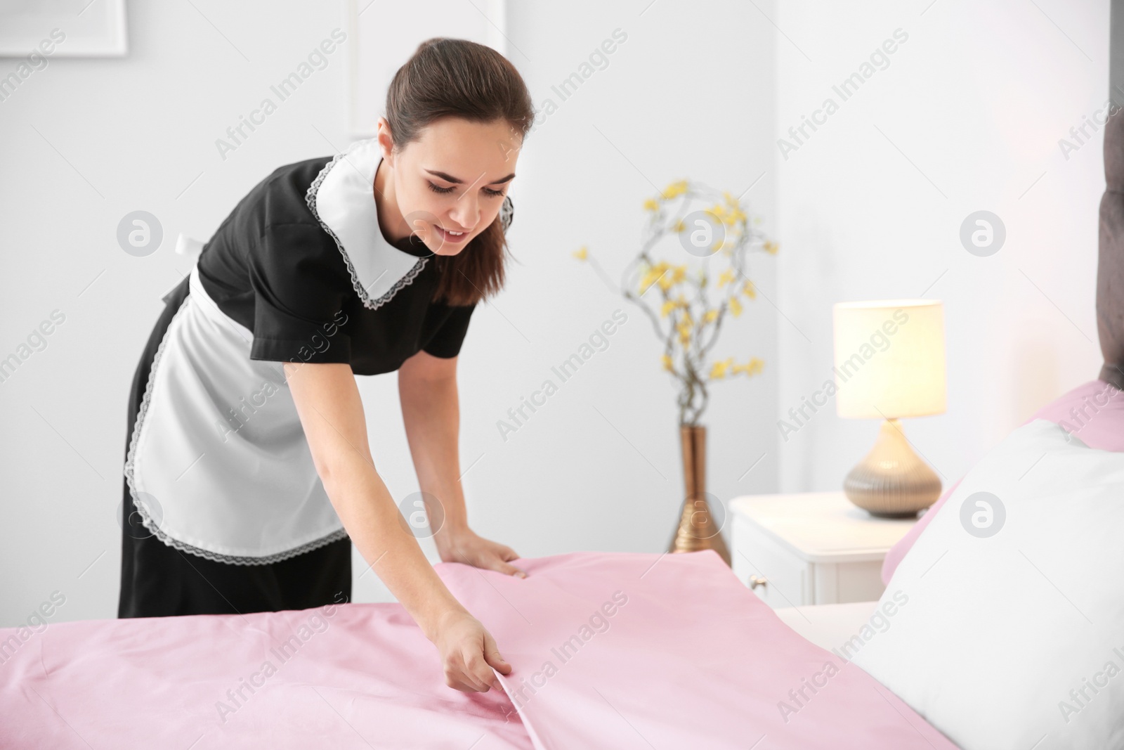 Photo of Young maid making bed in hotel room