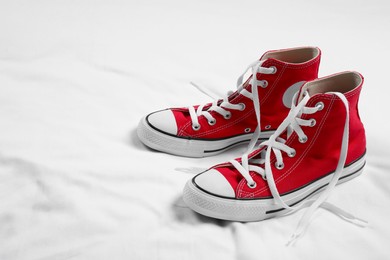 Pair of new stylish red sneakers on white fabric. Space for text