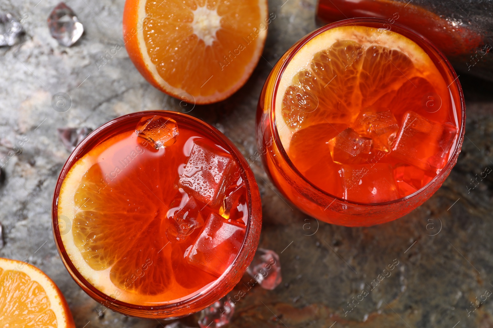 Photo of Aperol spritz cocktail, ice cubes and orange slices in glasses on grey textured table, top view