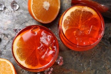 Photo of Aperol spritz cocktail, ice cubes and orange slices in glasses on grey textured table, top view