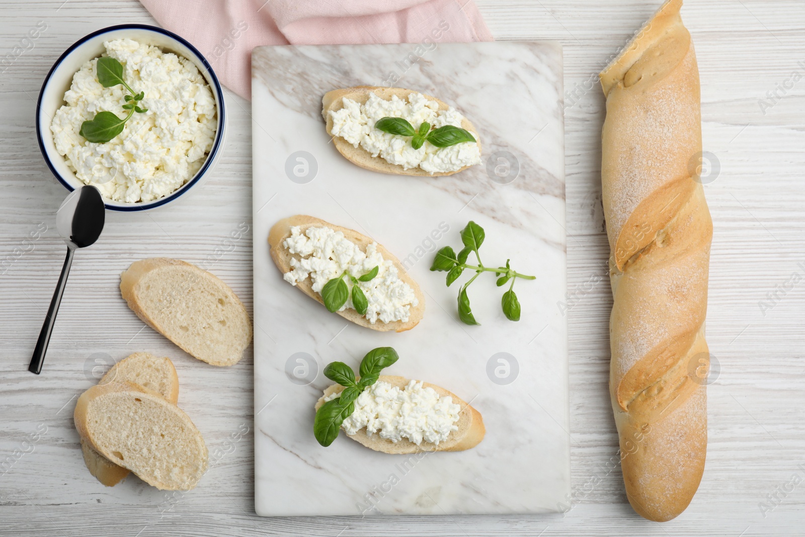 Photo of Bread with cottage cheese and basil on white wooden table, flat lay