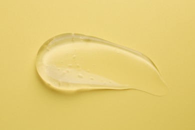 Photo of Smear of clear cosmetic gel on yellow background, top view