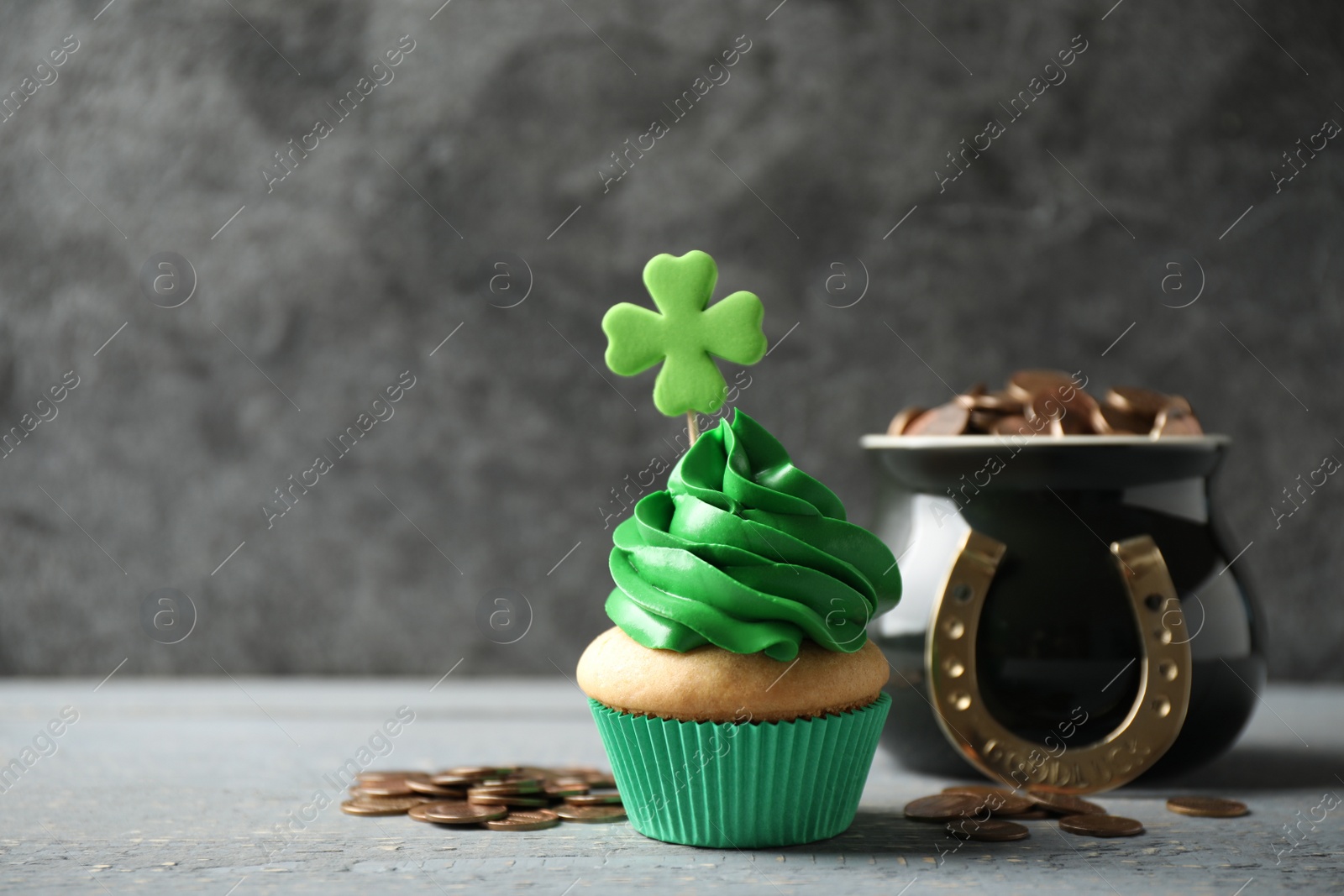 Photo of Decorated cupcake and pot with gold coins on grey wooden table, space for text. St. Patrick's Day celebration