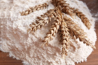 Photo of Pile of wheat flour and spikes on wooden board, top view